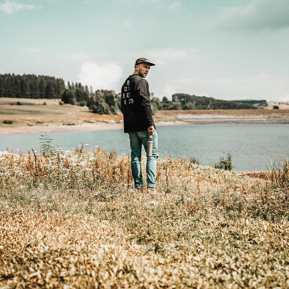 Mann in der Natur am See mit Trinkflasche aus Glas
