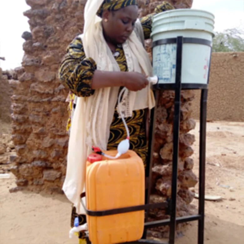Frau in Afrika zapft Wasser aus Wasserfilteranlage von faircap