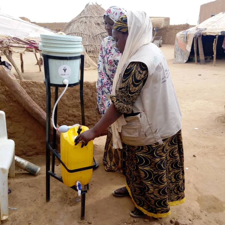 Frau in Afrika zapft Wasser aus Wasserfilteranlage von faircap